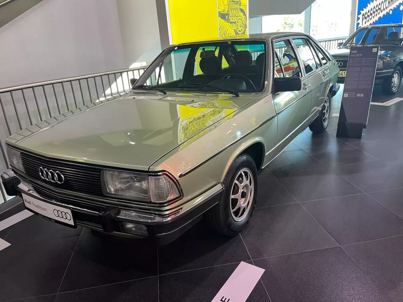 Двигун 2144 см³, рядний 5-циліндровий, впорскування Bosch K-Jetronic Потужність 136 к.с. (100 кВт) Розгін 0–100 км/год 9,5 с Максимальна швидкість 190 км/год Порядок роботи циліндрів 1-2-4-5-3, запалювання кожні 144° кута повороту колінвала Дебют / початок поставок серпень 1976 / березень 1977 Випуск Audi 100 C2 851 126 шт. (1976–1982) Саме з цього автомобіля почалася історія, якій присвячено всю виставку. У серпні 1976 року Audi представила друге покоління Audi 100 (C2, внутрішнє позначення Typ 43), а разом із ним — рядний п'ятициліндровий мотор. Поставки Audi 100 5E клієнтам почалися в березні 1977 року. Експонат у Audi museum mobile — седан кольору світло-зелений металік на легкосплавних дисках, із табличкою Audi Tradition замість номера. Сьогодні цей відтінок виглядає майже ніжно, але він чудово передає настрій кінця 1970-х. Індекс 5E розшифровується просто: п'ять циліндрів і впорскування палива, по-німецьки Einspritzung. Чому саме п'ять? Новий Audi 100 мав позиціонуватися вище за попередника. Як пояснює Audi, інженери порівнювали п'ятициліндровий і шестициліндровий рядні мотори, але від шістки відмовилися через брак місця в моторному відсіку та невигідний розподіл маси. Основою став чотирициліндровий EA 827 з Audi 80 зразка 1972 року, а п'ятициліндровий бензиновий мотор отримав позначення EA 828. Сама схема на той час була відома, але в масовому автомобілебудуванні майже не застосовувалася. Audi фактично зробила ставку на нішеву ідею — і не прогадала: через пів століття п'ять циліндрів стали однією з найвпізнаваніших рис марки. Технічно 5E виглядав переконливо: робочий об'єм 2144 см³, механічне впорскування Bosch K-Jetronic, 136 к.с. (100 кВт), розгін до 100 км/год за 9,5 с і максимальна швидкість 190 км/год. Відстань між осями циліндрів становить 88 мм, хід поршня — 86,4 мм. Але найцікавіше — порядок роботи циліндрів 1-2-4-5-3, який і дав назву виставці. Запалювання відбувається кожні 144° кута повороту колінчастого вала, і через непарну кількість циліндрів мотор звучить особливо: не так рівно, як шістка, і не так буденно, як четвірка. Цей хрипкуватий тембр шанувальники Audi впізнають із закритими очима. Покоління C2 випускали до серпня 1982 року. За даними Wikipedia, за цей час зібрали 851 126 автомобілів Audi 100 і ще 51 282 Audi 200 — разом понад 900 тисяч. Але справжнє значення 5E не в тиражі. Цей мотор відкрив шлях до першого п'ятициліндрового дизеля, до турбованого Audi 200 5T, до легендарного quattro і зрештою до сучасних RS-моделей. Тому на виставці світло-зелений седан стоїть на почесному місці: усе, що відвідувач побачить далі, — від Avant RS2 до Audi RS 3, — є прямим нащадком цього спокійного на вигляд автомобіля.