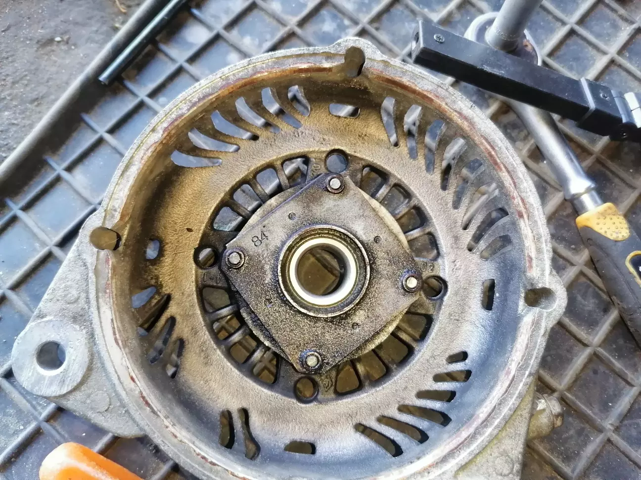 Передній підшипник закрито металевою пластиною. Щоб її зняти треба ударною викруткою відкрутити 4 болтика. Лупити с дуру непотрібно. Під кришку треба шось підкласти, щоб не зламати кришку генератора.